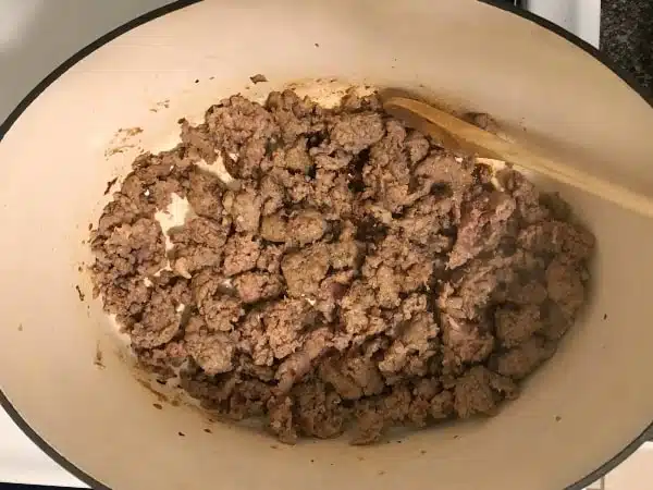 Browned sausage in dutch oven with wooden spoon