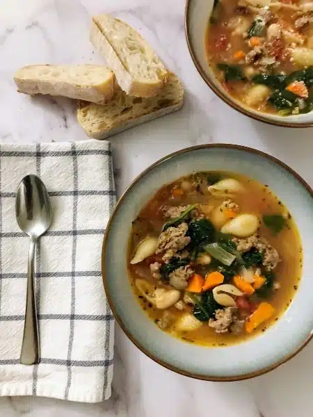 Italian Sausage and Vegetable Soup in a bowl with bread, spoon, and napkin