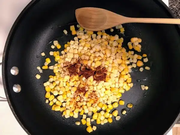 Corn in skillet with chili powder to prepare for avocado toast with tomatoes and corn
