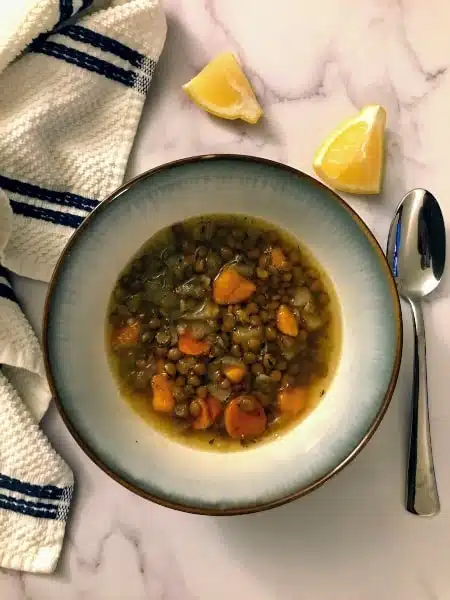  lentil soup with vegetables in a bowl with a spoon and 2 lemon slices on the side