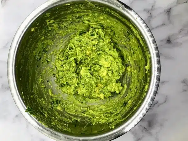 metal bowl with mashed avocado, lime juice, cilantro, and salt, to get ready to spread for avocado toast with tomatoes and corn