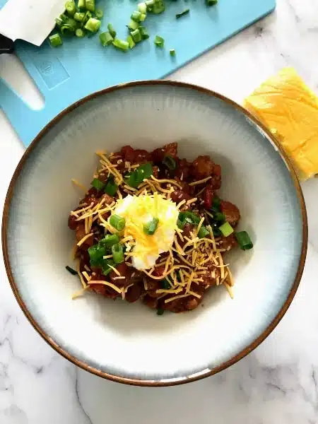 Slow Cooker Turkey Chili in a bowl with cornbread and sliced green onions on a cutting board