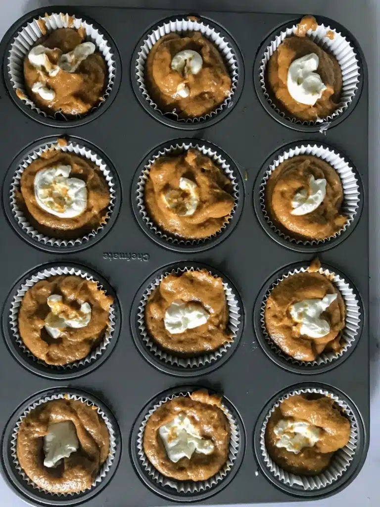 pumpkin muffin batter with cream cheese in muffin tin.