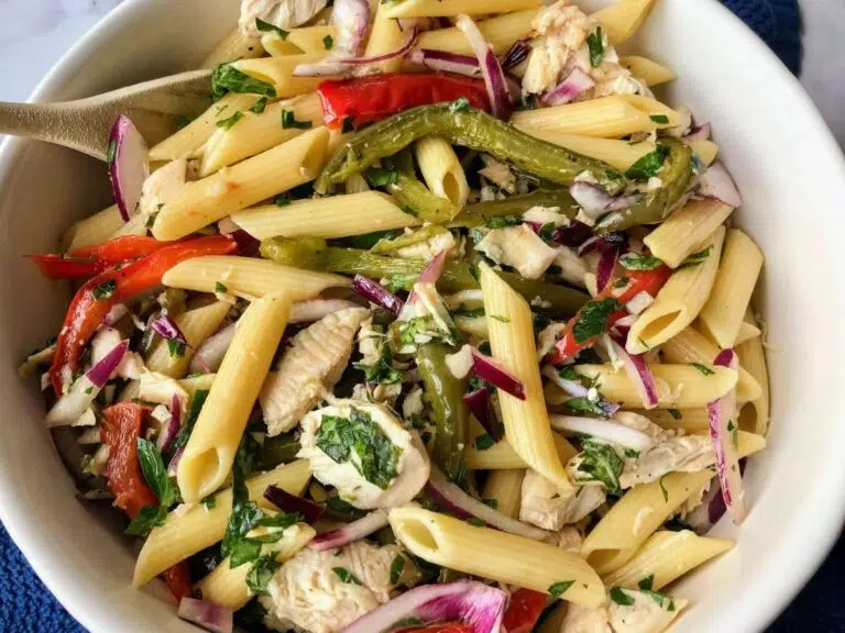 chicken bell pepper pasta salad in a white bowl with a wooden spoon.