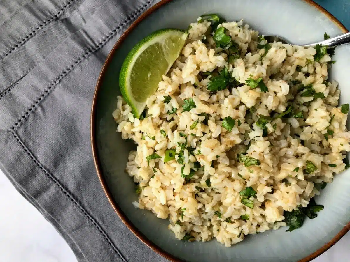 Bowl of brown rice with chopped cilantro and a lime wedge.