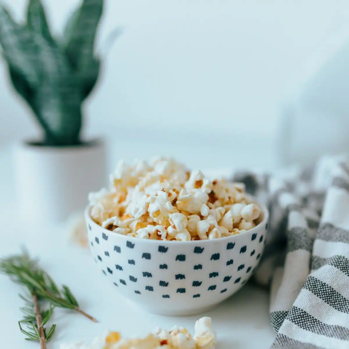 popcorn in a bowl with rosemary sprigs on the side.