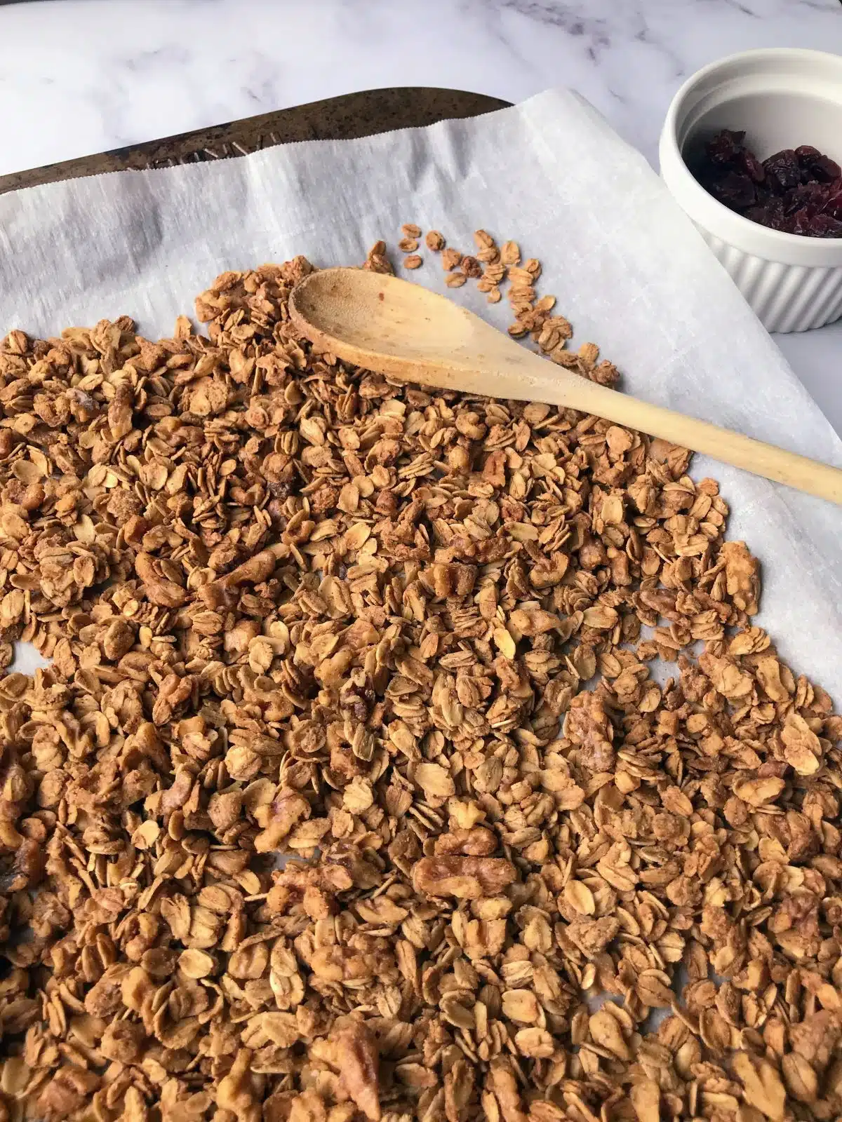 Baked granola on a baking sheet with a wooden spoon.