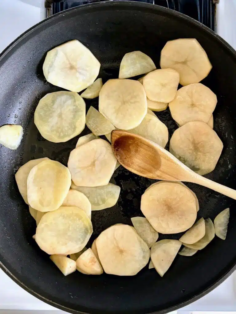Sliced potatoes sautéing in a skillet.