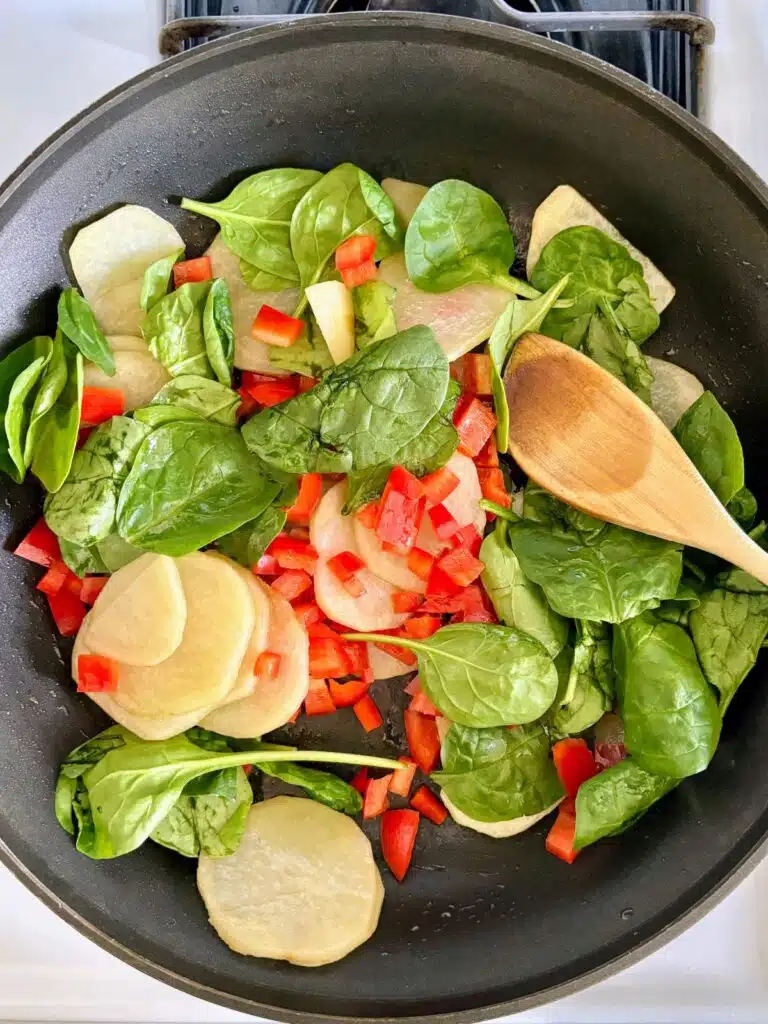 Potatoes, spinach, and red bell peppers cooking in a skillet.