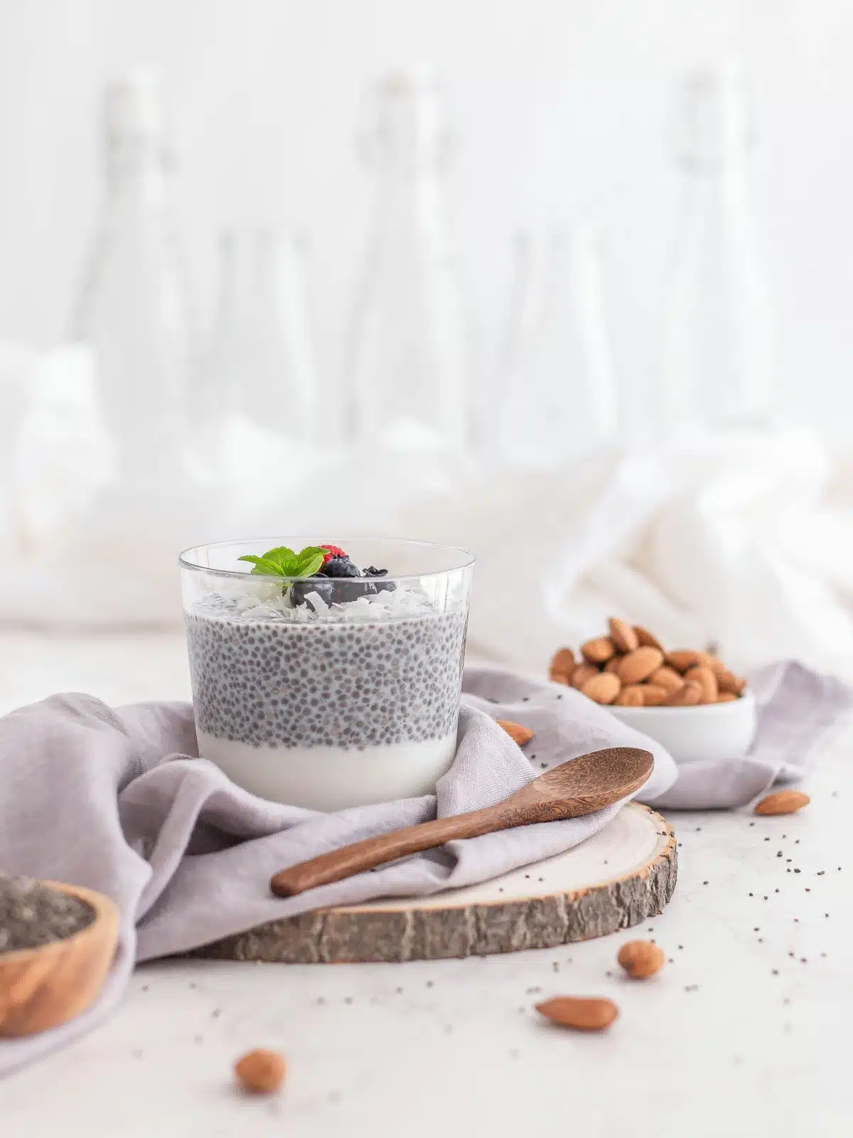 Chia seed pudding in a glass cup next to a bowl of almonds and a wooden spoon. 