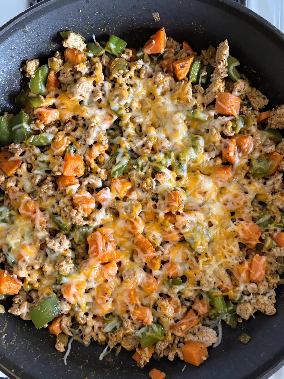 Melting cheese on turkey and vegetables in a skillet.