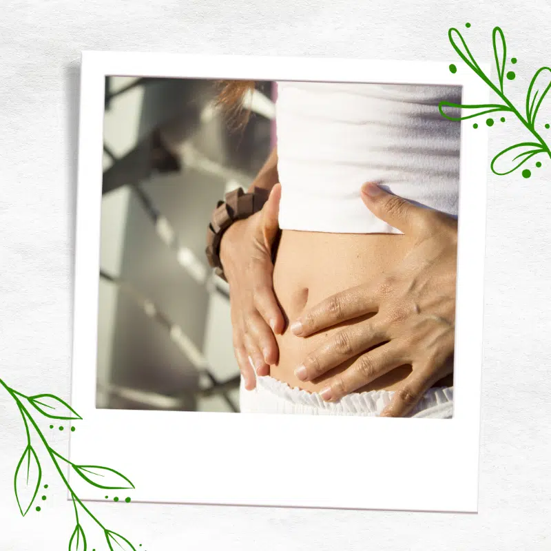 woman with abdomen showing and has her hands on her abdomen.